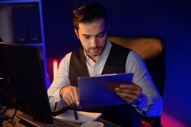 Stresli akıllı işadamı, gece geç saatlerde Mor Neon Koyu Işık Odası 'ndaki disiplin ürünleri servisinin çevrimiçi satış kanalını oluşturmak için kağıt işi raporu klasöründeki pazar verilerini analiz ediyor. Tahmin et..