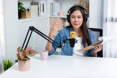 Sosyal medyada kulaklıkla canlı yayın yapan Asyalı sunucu modern stüdyoda yaşam koçluğu veya pazarlama dinleyicilerini selamlıyor. Taktik.