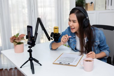 Asyalı sunucu canlı yayında canlı yayında canlı yayında sosyal medyada kulaklık takarak konuşuyor. Dinleyicileri modern stüdyoda koçluk yaparak selamlıyor. Taktik.