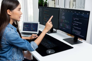 İnternet sitesinde kodlama programı uygulaması olan ve kot gömlek giyen bilgisayar hakkında bilgi veren IT geliştiricisi genç bir Asyalı kız. Güvenlik programlarıyla çevrili iki ekran. Taktik.