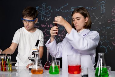 Öğretmen, laboratuarda öğrenciyi destekliyor. Öğrenci ve öğretmen cam kapta sıvı kullanarak STEM sınıfında kimya bilimi üzerine deney yapıyorlar. Karıştırma çözeltisi. Etkinlik.