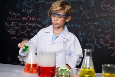 Laboratuvardaki sarışın çocuk laboratuvar önlüğü giyer ve STEM sınıfında kimya bilimi öğrenir. Öğrenci cam şişeye sıvı döker. Masaya bir sürü şişe koy. Etkinlik.