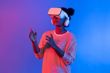 Kullanıcı deneyiminde VR ile sunum yapan genç Afrikalı bir kadın, üç boyutlu teknoloji yenilikçiliği hologram teknolojisi uygulamasındaki çevrimiçi neon stüdyo ışıklandırma arka planı aracılığıyla sunuluyor. Entrika.