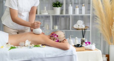 Sıcak bitkisel top spa masaj vücut tedavisi, masör kadın vücuduna nazikçe şifalı bitki torbası bastırıyor. Aromaterapi dinlenme sükuneti ve sükuneti kaplıca salonundaki atmosferi aydınlatıyor. Sessiz.