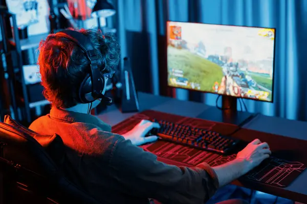 Stock image Host channel of young gaming streamer, team gamer playing battle game shooting with multiplayer at warship on pc screen with back side image, wearing headset with mic at digital neon room. Gusher.