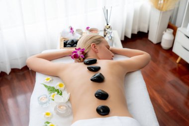 Lüks tatil köyündeki kaplıcalarda sıcak taş masajı. Gün ışığı sükunet ortamında, mutlu kadın müşteri bazalt taş masajından zevk alıyor. Rahatlatıcı bir sıcaklıkla vücudun üzerinde süzülüyor. Sessiz.