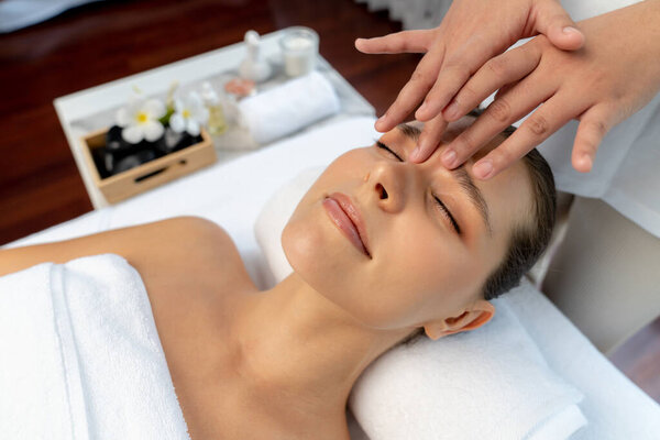 Caucasian woman enjoying relaxing anti-stress head massage and pampering facial beauty skin recreation leisure in dayspa modern light ambient at luxury resort or hotel spa salon. Quiescent