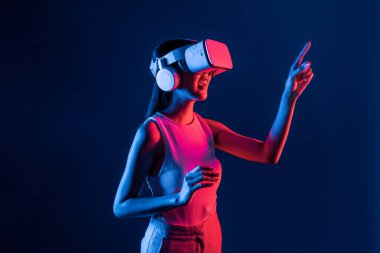 Siberpunk neon ışıklı cihazlarla çevrili zeki bir kadın metaevrene bağlı VR kulaklık takıyor, gelecekçi siber uzay teknolojisi. Sanal objeyi işaret eden bir kadın. Halüsinasyon.