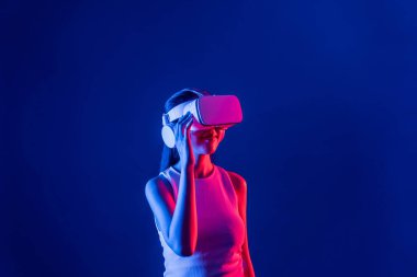 Siberpunk neon ışıklı cihazlarla çevrili zeki bir kadın metaevrene bağlı VR kulaklık takıyor, gelecekçi siber uzay teknolojisi. Zarif bir kadın sanal ortamda yaratılmış gibi görünür. Halüsinasyon.