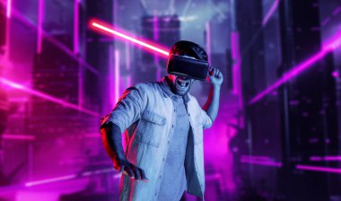 Lazer kılıcı tutan ve VR gözlük takan oyuncu. Beyaz adam, neon şatonun etrafında dikilirken görsel gerçeklik kulaklığı kullanıyor. Yenilik teknolojisi. Sapma.