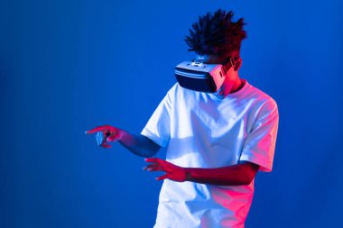 Sanal gerçeklik dünyasını dijital fütüristik teknolojiye bağlayan mavi pembe ışık duvarını gösteren 3 boyutlu hologram gösteren genç bir Afro-Amerikan oyun oyuncusu. Entrika.