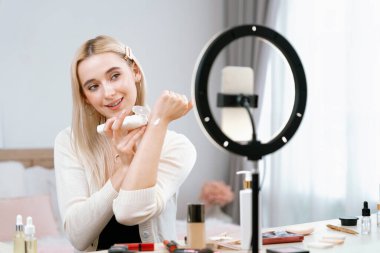 Sosyal medya için güzellik ve kozmetik video içeriği hazırlayan genç bir kadın. Güzellik blogcusu kameraya gülümserken seyirciye ya da takipçilere güzellik teninin nasıl uygulanacağını gösteriyor. Blithe