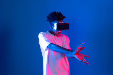 Sanal gerçekliği dijital fütüristik teknolojiye bağlayan pembe mavi neon duvarda VR 'dan bakan genç Afrikalı Amerikalı' ya şaşırdım. Entrika.