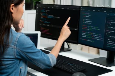 İnternet sitesinde kodlama programı uygulaması olan ve kot gömlek giyen bilgisayar hakkında bilgi veren IT geliştiricisi genç bir Asyalı kız. Güvenlik programlarıyla çevrili iki ekran. Taktik.