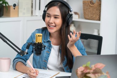 Sosyal medyada kulaklıkla canlı yayın yapan Asyalı sunucu modern stüdyoda yaşam koçluğu veya pazarlama dinleyicilerini selamlıyor. Taktik.