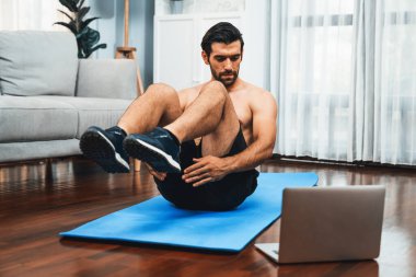 Atletik ve sporcu adam spor paspası üzerinde çatırdarken evdeki formda fiziğe ve sağlıklı spor yaşam tarzına uygun online ev eğitimi takip ediyor. Çevrimiçi neşeli ev egzersizi videosu.