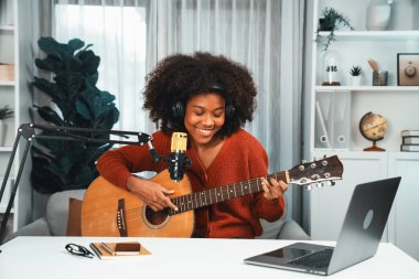 Genç Afrikalı Amerikalı müzisyenin sunucu kanalı gitar çalıyor, şarkı söylüyor, stüdyoda dizüstü bilgisayardan yayın yapıyor. Kulaklık dekorasyonu ve mikrofon kaydı. Tatlandırıcı.