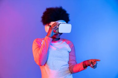 Genç Afrikalı, teknolojik dijital yenilik grafiğinde mavi neon aydınlatma grafiğinde izole edilmiş 3 boyutlu hologram veri uygulamasını seçmek için metaevren üzerinden VR gözlük takıyor. Entrika.