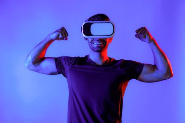 Sanal gerçeklik gözlüklü mutlu bir adam neon ışıklı arka planda kaslarını esnetiyor. Sıradan kıyafet giyen, sanal gerçeklik simülatörü teknolojisi kullanarak rahatlayan ve egzersiz yapan sağlıklı bir insan. Sağlıklı temsil et. Sapma.