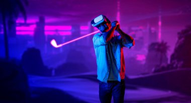 Sanal dünyaya girmek için sanal gözlük takan beyaz bir adam metaevrende golf oynuyor. Sanal gerçeklik gözlüğü kullanan yakışıklı oyuncu neon golf sahasına giriyor. Yenilik. Spor. Sapma.