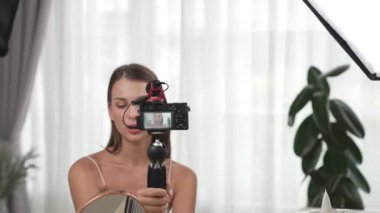 Sosyal medya için güzellik ve kozmetik video içeriği hazırlayan genç bir kadın. Güzellik blogcusu kameraya gülümserken seyircilere ve takipçilere güzellik bakımını gösteriyor. Düzenle