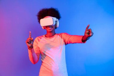 Genç Afrikalı, mavi pembe neon aydınlatma grafikli dijital yenilik 3 boyutlu hologram gramında veri öğrenme uygulaması ile metaevren boyunca VR gözlük takıyor. Entrika.