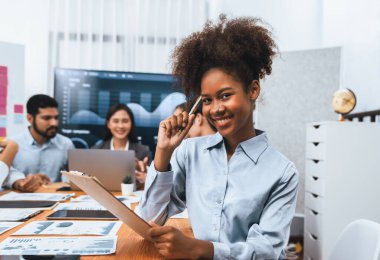 Bir grup ofis çalışanı ile birlikte arka planda ekranda gösterim paneliyle buluşan mutlu Afrikalı genç bir iş kadını portresi. Takım toplantısında kendine güveni tam bir ofis hanımı. Uyum