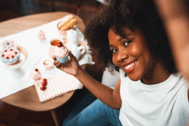 Genç ve güzel Afrikalı blogcu akıllı telefondaki selfie ile konsept özel mutfak konseptinde kek sunuyor. Favori tatlı fırın yemeğiyle sosyal medyanın yaratılması. Tatlandırıcı.