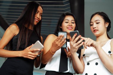 Üç kadın arkadaş ellerinde cep telefonuyla sohbet ediyorlar. Sosyal medya, dedikodu haberleri ve online alışveriş kavramı. uds