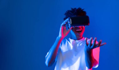 Sanal gerçekliği dijital fütüristik teknolojiye bağlayan pembe mavi neon duvarda VR 'dan bakan genç Afrikalı Amerikalı' ya şaşırdım. Entrika.