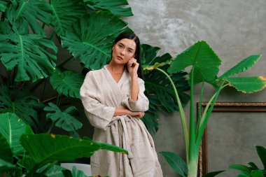 Modern otelde küveti olan tropikal ve egzotik bir spa bahçesi ya da yemyeşil yeşillik arka planıyla çevrili rahat ve sağlıklı yaşam tarzının tadını çıkaran bornozlu bir kadınla tatil köyü. Blithe