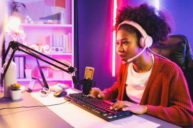 Neon renkli aydınlatma odasında kulaklık takan Afrika kökenli Amerikalı kız flamalı Esport yetenekli takımıyla online dövüş yapıyor. Rakiplerini kazanmak için strateji planlayan diğer oyuncularla konuşmak. Tatlandırıcı.