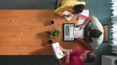 Renk paletinden renk seçmek için birlikte çalışan iş adamlarının üst düzey hava görüşü. İşadamı logo grafiğine bakarken pazarlama ekibine tablet kullanarak yönetici fikri sundu. Sempozyum.