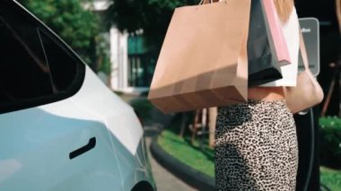 Yavaş çekimde genç bir kadın, alışveriş merkezinden şehir merkezine veya sürdürülebilirlik yeşil ve temiz elektrikli taşıtlara sahip apartman dairesine döndükten sonra EV elektrikli otomobilini şarj ediyor.