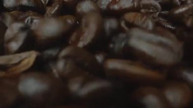 Karışık aromalı kahve çekirdeği yığını masaya saçılmış ve kavrulmuş kahve çekirdekleri etrafa saçılmış siyah arkaplanla çevrilmiş. Makrografi. Ağır çekim. Pabulum.