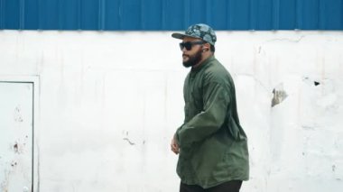 Sokak ortasında mavi duvarlı hippi dansçı ayak basamağı. Asyalı break dansçı kollarını açarken sokak dansı yapıyor. Hip hop koreografı enerjik bir dans sergiliyor. Açık hava sporu 2024 hiphop..