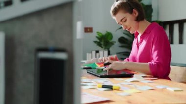 Tablet ekran logosu tasarımı ile toplantı masasında otururken renkli yapışkan notlar üzerine tasarımcı yazma fikrinin üst görünümü. Tasarım yapan ve karar veren profesyonel bir iş kadını. Sempozyum.