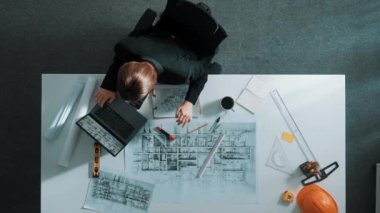 Dizüstü bilgisayarda çalışırken mimari çizimlerin hava görüntüsü. Kafkasyalı mühendisin bina modelini tasarlayıp, ekipman ve güvenlik kaskıyla birlikte tasarladığına dair tepeden aşağı bir bakış açısı. Hizalama.