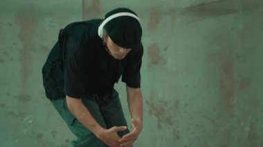 Kulaklıktan çimento arka planda müzik dinlerken break dans pratiği yapan yakışıklı bir hippi. Yakışıklı Asyalı sokak dansçısı robot dansı yapıyor. Açık hava sporu 2024. Modern dans. hiphop.