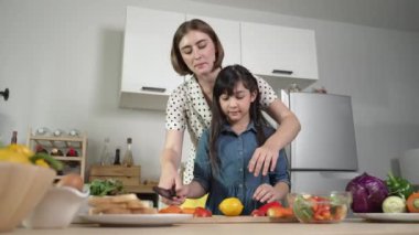 Zeki beyaz anne ve Asyalı kız birlikte yemek pişiriyor ve sebze doğruyor ya da akşam yemeği için salata hazırlıyor. Mutlu anne ve kız taze yemekle sağlıklı yemek yapıyorlar. Sağlıklı gıda konsepti. Pedagoji.