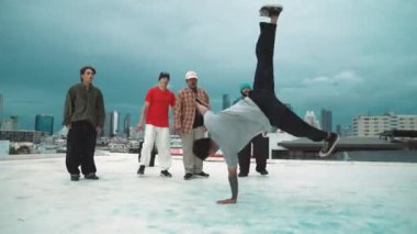 Profesyonel hippi hareketsiz poz verirken aynı zamanda şehir manzaralı çatıdaki müziğe ayak basıyor. Break dansçı, hip-hop dansçıları grubuyla birlikte sokak dansı yapıyor. Açık hava sporu 2024 hiphop..