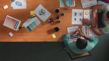 Proje yöneticisi renk paletleri seçerken tasarımcının tablete baktığı yukarıdan aşağıya hava görüntüsü. Profesyonel grafik tasarımının en üst görüntüsü ve logoya bakın. Yetenekli ekip grafikleri seçiyor. Sempozyum.