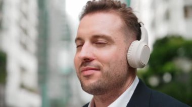 İş adamlarının kulaklıklarını kapat ve neşeli ve motive edici bir şekilde müzik eşliğinde dans et. Yetenekli proje yöneticisi şehir merkezinde bulanık arkaplanlı rahat şarkılar dinlemeyi sever. Urbane.