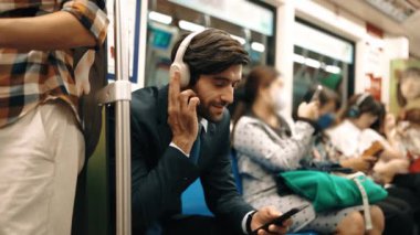 Gülümseyen yakışıklı yatırımcı trende otururken rahatlatıcı müzik dinliyor. Profesyonel iş adamı iş yerine toplu taşıma araçlarıyla giderken müzik dinlemeyi sever. Arka plan bulanık. Sevinçli..