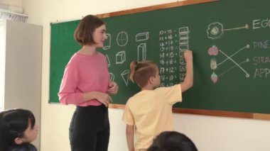 Tebeşir alırken ve ilkokulda teoriyi açıklarken sınıfta matematik sorusunu cevaplamak için karatahta yazan beyaz öğrenci. Çeşitli çocuklar matematik dersinde öğreniyor ve çalışıyor. Pedagoji.