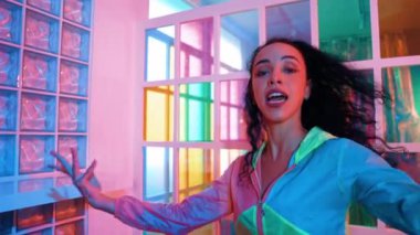 Neşeli İspanyol kız gece kulübünde renkli giysiler giyerken neon ışıkta müzik eşliğinde hareket ediyor. Sokak dansçısı kameraya bakarken hareketli adımlar atıyor. Mutluluk.