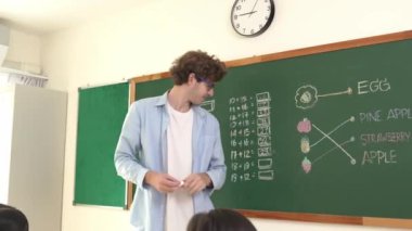 Öğrenciye bakarken, sınıfta matematik teorisi hakkında konuşan ve açıklayan beyaz bir öğretmen. Tahtanın önünde durup tahtaya işaret eden yetenekli bir eğitmen. Pedagoji.