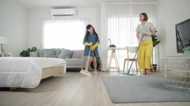 Beyaz anne ve Asyalı çocuk birlikte ev işi yapıyor ve müzik eşliğinde dans ediyorlar. Çekici anne ve kız modern yatak odasını temizlerken şarkı söyleyip rahatlatıcı müziğe atlıyorlar. Yaşam tarzı. Pedagoji.