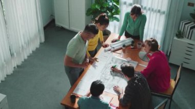 İnşaat mühendisi ekibinin renkli paletlerle toplantı masasında plan yazışının en üst görüntüsü. Yönetici proje planlarına bakarken bir grup zeki insan plan yapıyor ve not alıyor. Sempozyum.