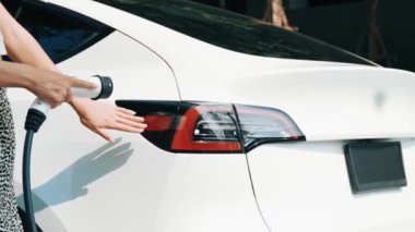 Yavaş çekim kadın, yeşil sürdürülebilir şehir parkı bahçesinde şarj olan EV elektrikli arabasıyla geziyor. Sürdürülebilir kentsel yaşam tarzında, yeniden şarj edilebilir elektrikli araç iç organlarıyla alışverişe gidiyor.